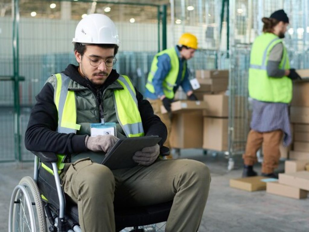 jovem-trabalhador-serio-de-armazem-sentado-em-cadeira-de-rodas-e-usando-tablet_274679-44792