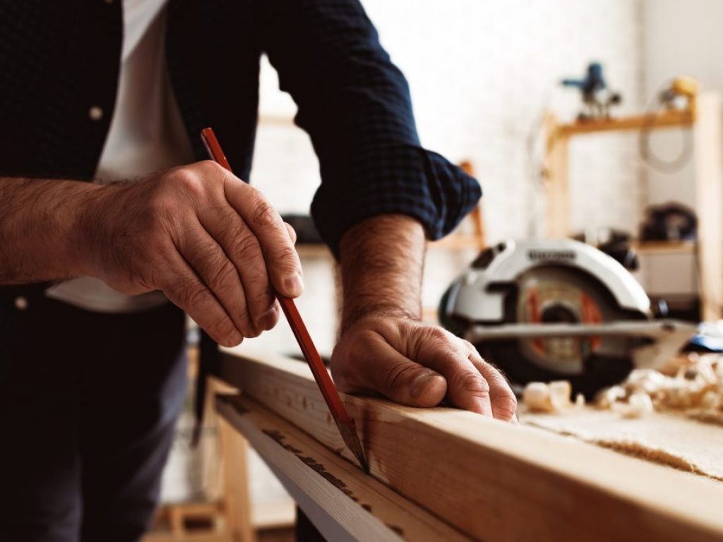 Carpenter makes pencil marks on a wood plank