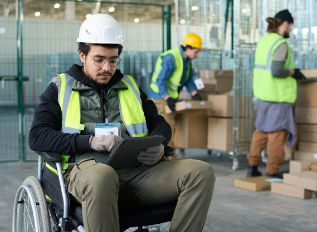 jovem-trabalhador-serio-de-armazem-sentado-em-cadeira-de-rodas-e-usando-tablet_274679-44792