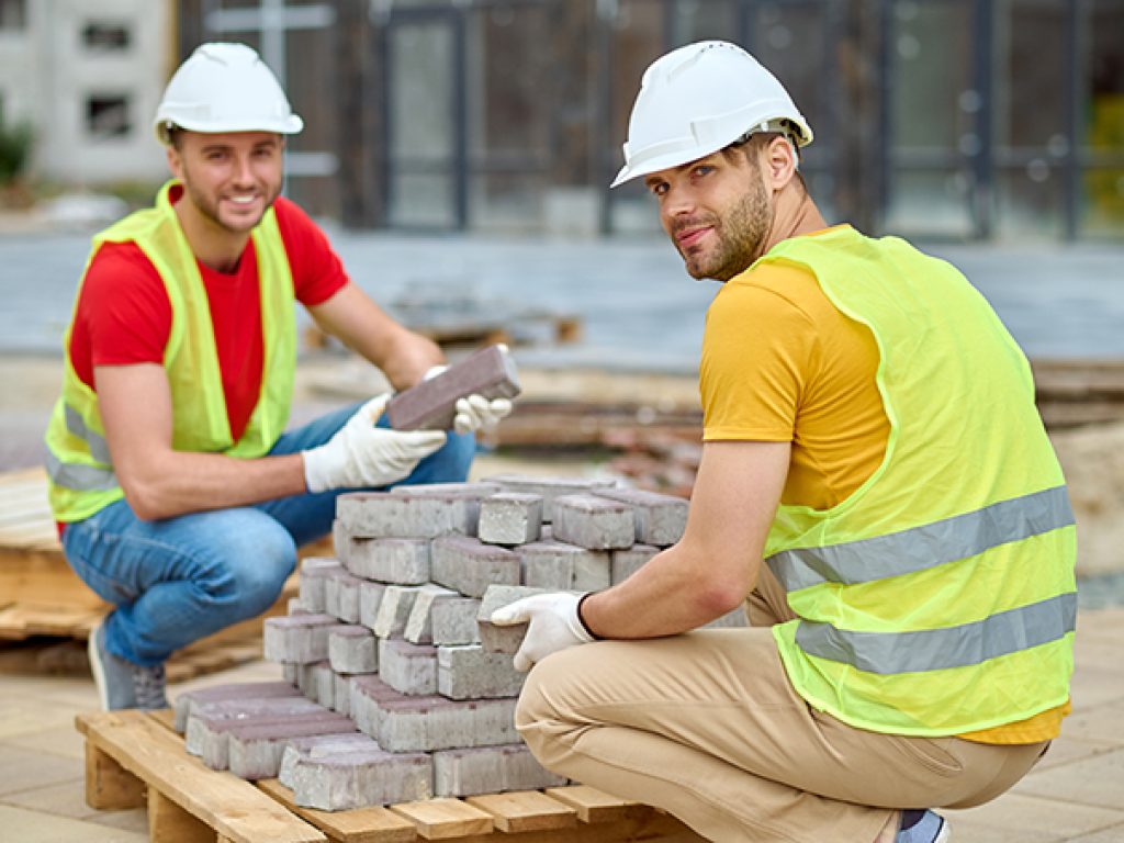 Two workers stacking bricks looking at camera