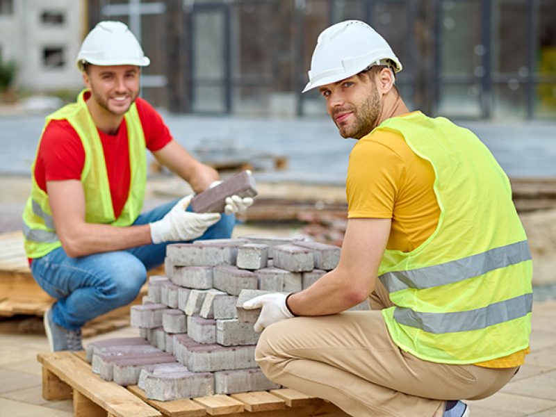 Two workers stacking bricks looking at camera